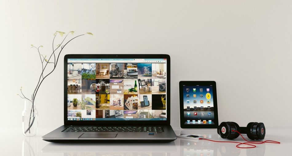 Laptop z wynajmu laptopa leży na stole wraz z tabletem, słuchawkami i wazonem