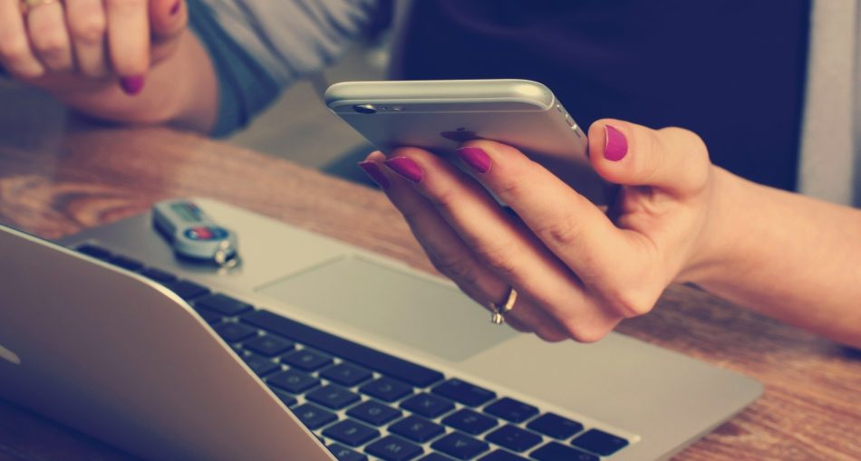 laptop z wypożyczalni laptopów; osoba siedzi przy laptopie; w ręku trzyma telefon